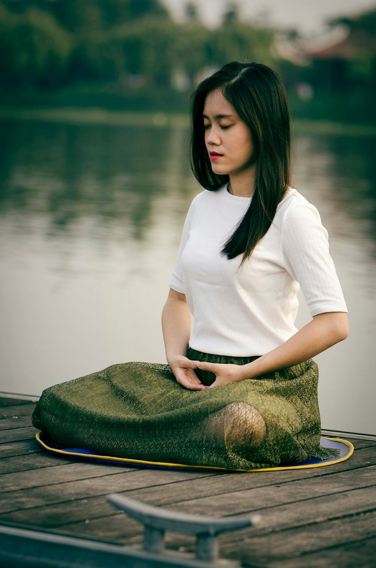 Woman sitting still and meditating on a wooden dock by the water
