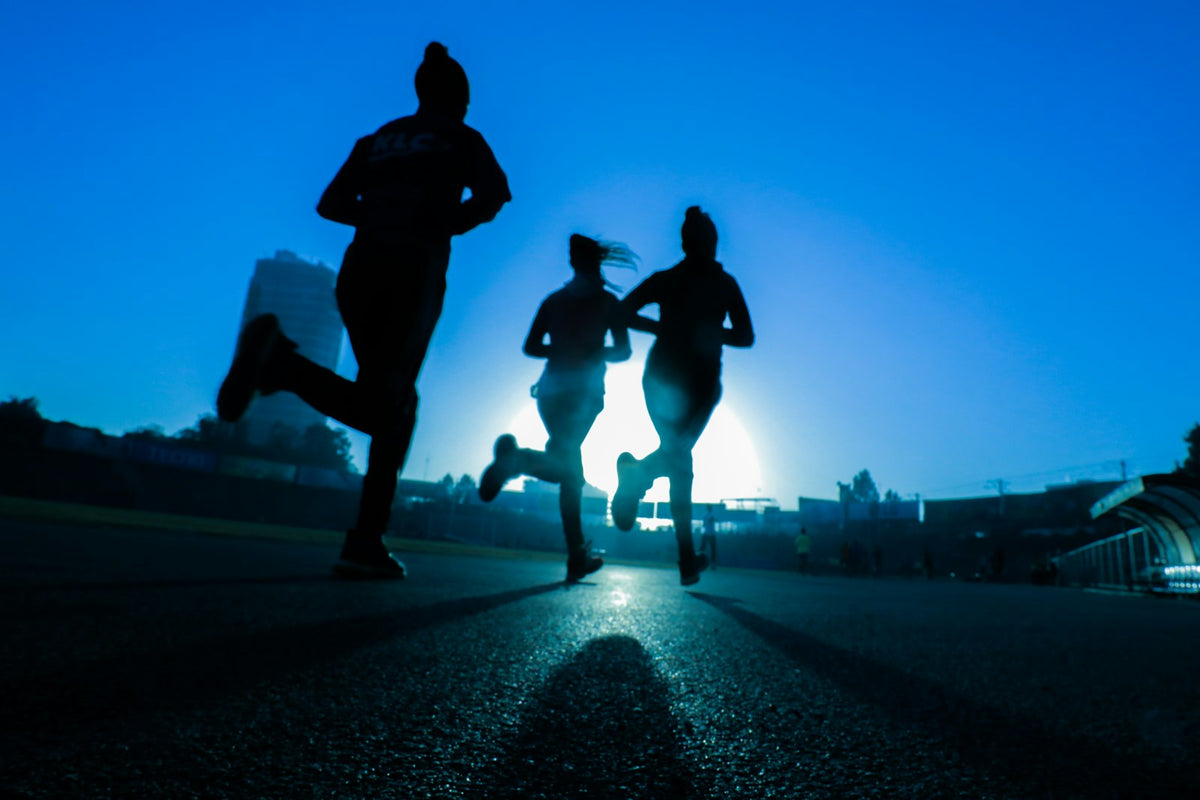 Silhouettes of three people running together on a road – team fitness and corporate wellness in the UAE