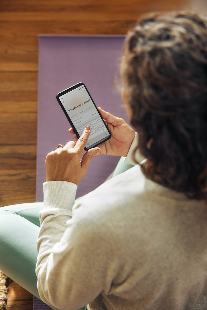 Woman checking her health and fitness app on a smartphone while sitting on a yoga mat